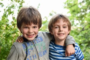 two brothers looking at the camera laughing while holding at each others in a park in france