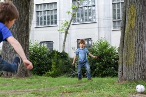 two young boys playing soccer in a park with the goal between two trees
