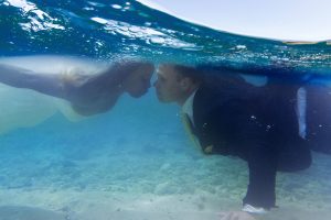 couple reaching to kiss underwater with wave over them in Fiji by Anais Photography