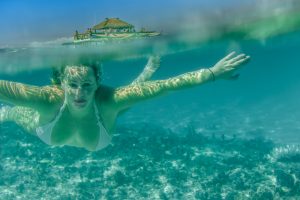 Over under shot with woman swimming toward the camera and Cloud 9 floating bar on the top in Fiji by Anais Photography