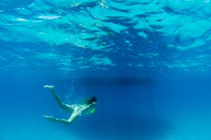 Woman swimming under pristine blue water of Fiji by Anais Photography