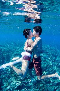 couple kissing and holding eachother underwater with corals in the ocean in Fiji by Anais Photography