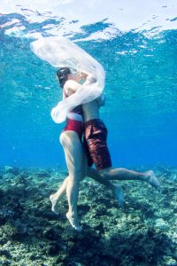 couple cuddling underwater with fabric turning around them in Fiji by Anais Photography