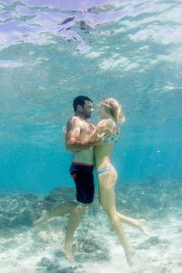 Couple holding eachother hugging in verticale position underwater Cloud 9 in the Mamanuca islands in Fiji