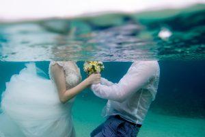 Couple holding hands and flowers underwater in Fiji for their trash the dress photoshoot