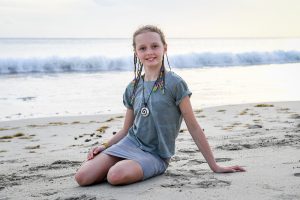 Cute young girl in braids seated on the beach in Fiji sunset