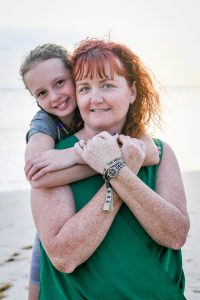 Braided daughter hugs neck of Red haired mum in Family beach photoshoot