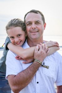 Braided daughter hangs on daddy's shoulder in family beach photography