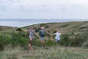 Cute brother and sister run in the countryside against ocean and sunset in Fiji family photoshoot