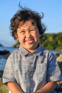 Cute curly haired boy sticks out his tongue at the beach in Malolo Fiji