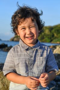 Cute curly haired boy laughs at the beach in family photo session