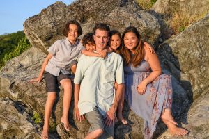 Cute mixed race family pose for a photoshoot against a rock in Fiji