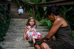 Mom puts shoes on her daughter at bottom of steps during family vacation