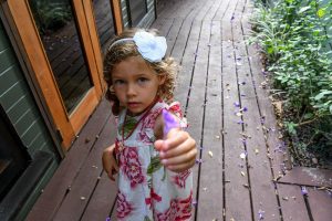 Cute little girl with flower in her hair offers camera a purple flower