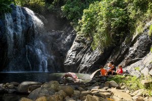 Family seated by river watching waterfall during family vacation in Fiji