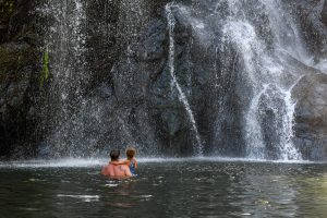 Dad and daughter wade towards waterfall in Tropical Fiji