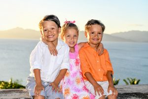 Triplets seated against the sunset smile at the camera in Fiji family vacation