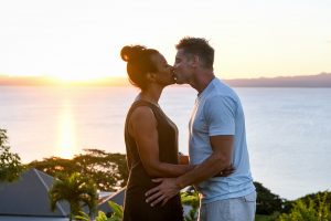 Mixed race caucasian and Polynesian couple kiss against sunset and the ocean in Fiji