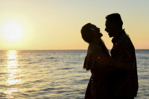 Mother and father are silhouetted as they laugh with the golden sunset behind them
