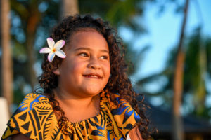 Sun-kissed daughter stares into the sea with frangipani flower in her hair