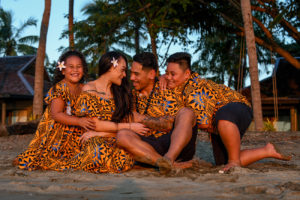 The family huddles on the beach with the sunset glowing off their skin at Double Tree Hilton Fiji
