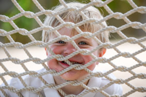 The cute baby grins at the camera through the hammock net