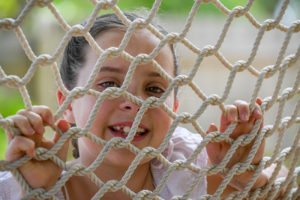 The cute little girl peers at the camera through the hammock net