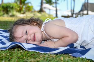 Cute baby girl lies down on a blue towel on green grass