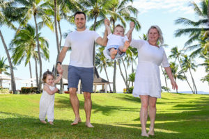 Mother and father lift baby off the ground against palm trees