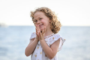 Cute wavy haired girl claps while on the beach