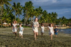 Cousins in white run on the beach against palm trees