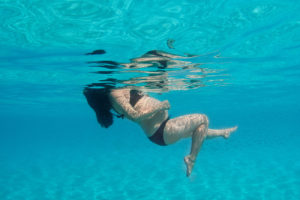 Fish fall behind as a lady kicks her legs in underwater pregnancy shoot