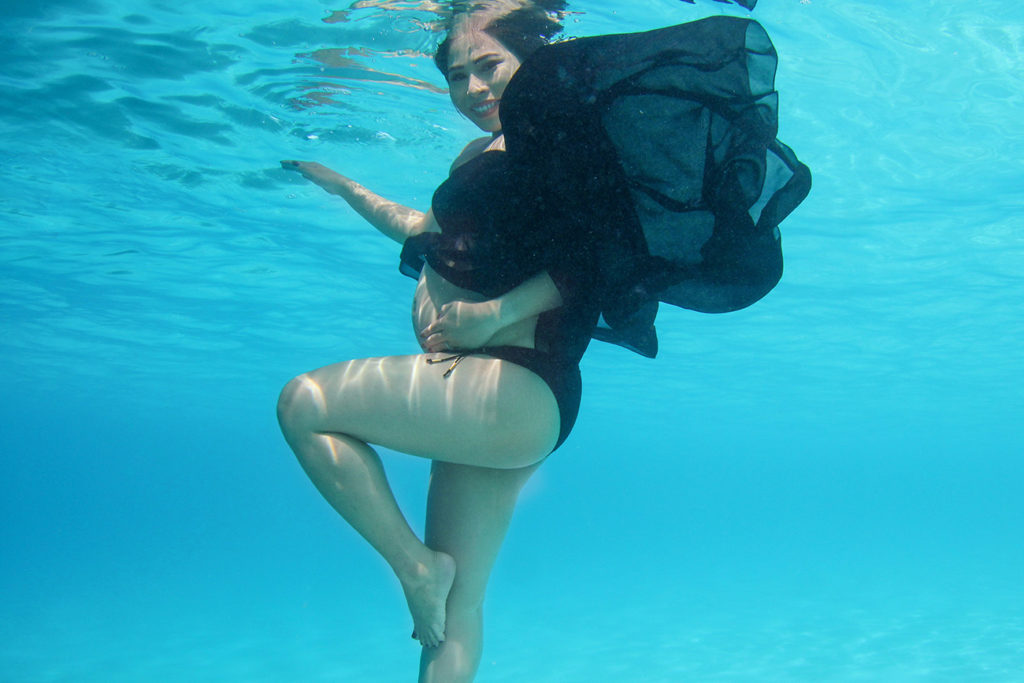 Pregnant mermaid wearing black floating underwater