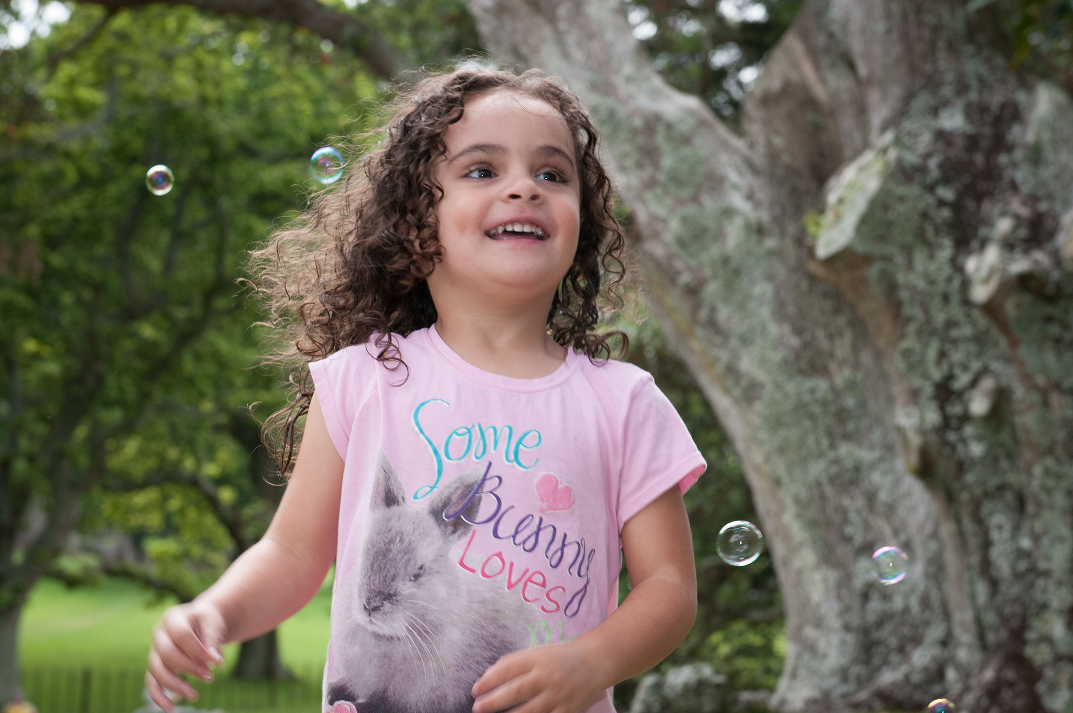 Young curly girl playing with bubbles in One Tree Hill Park, Auckland, New Zealand. Professional portrait by Anais Chaine Photographer