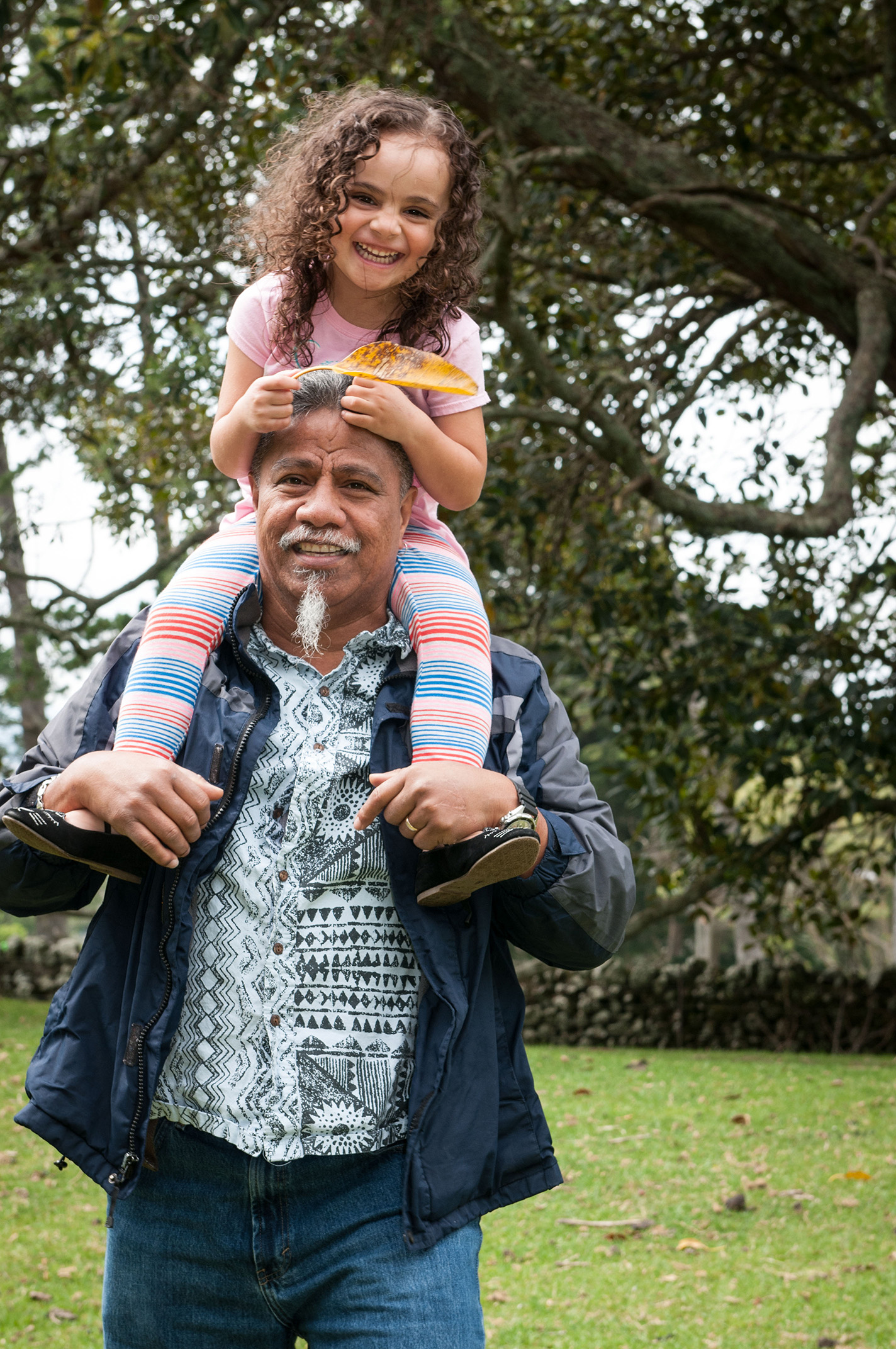 Young curly girl on her dad's shoulders in One Tree Hill Park, Auckland, New Zealand. Professional portrait by Anais Chaine Photographer