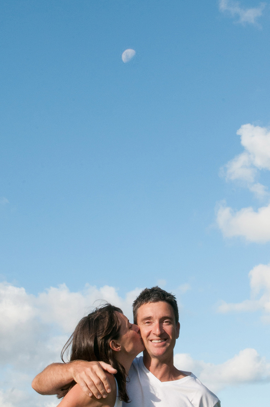 Couple, clouds, blue sky and moon in Point Chevalier, Auckland, New Zealand. Professional portrait by Anais Chaine Photography.
