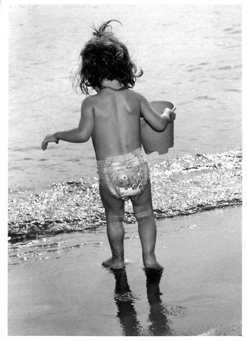 Little girl walking to the sea holding her bucket in Hyeres, south of France, French Riviera.