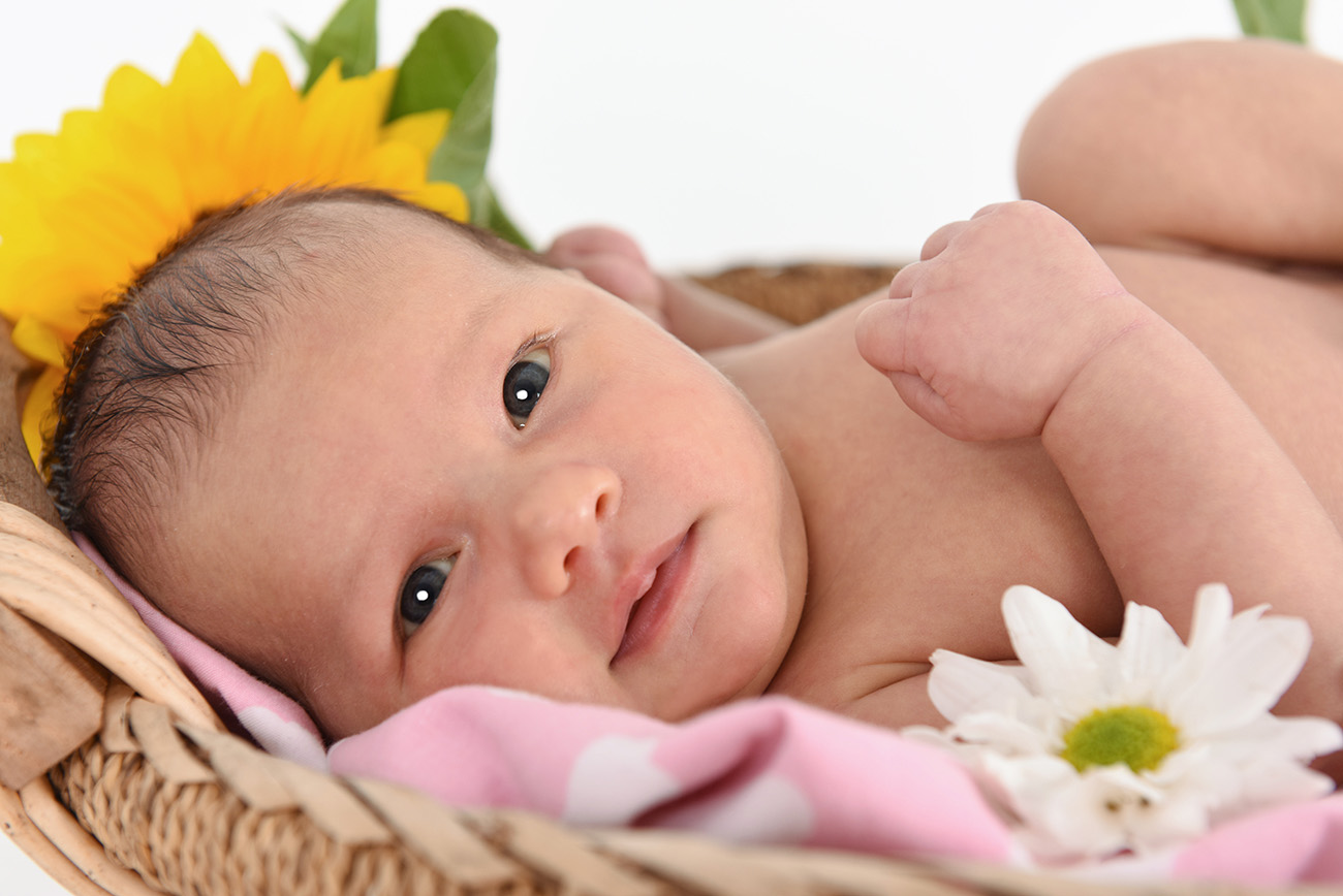 Half cropped of baby laying down in wicker basket with flowers