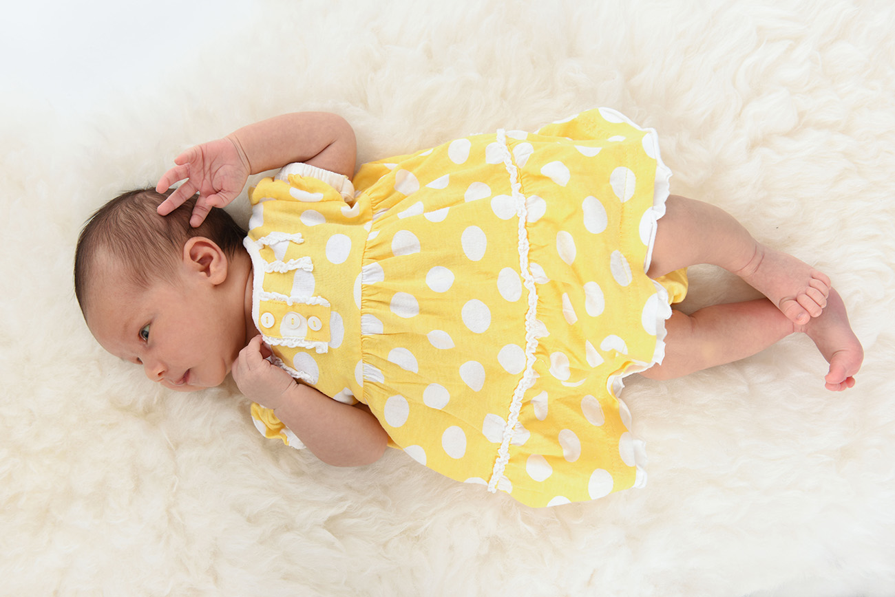Baby laying down her back in a beatiful yellow dress