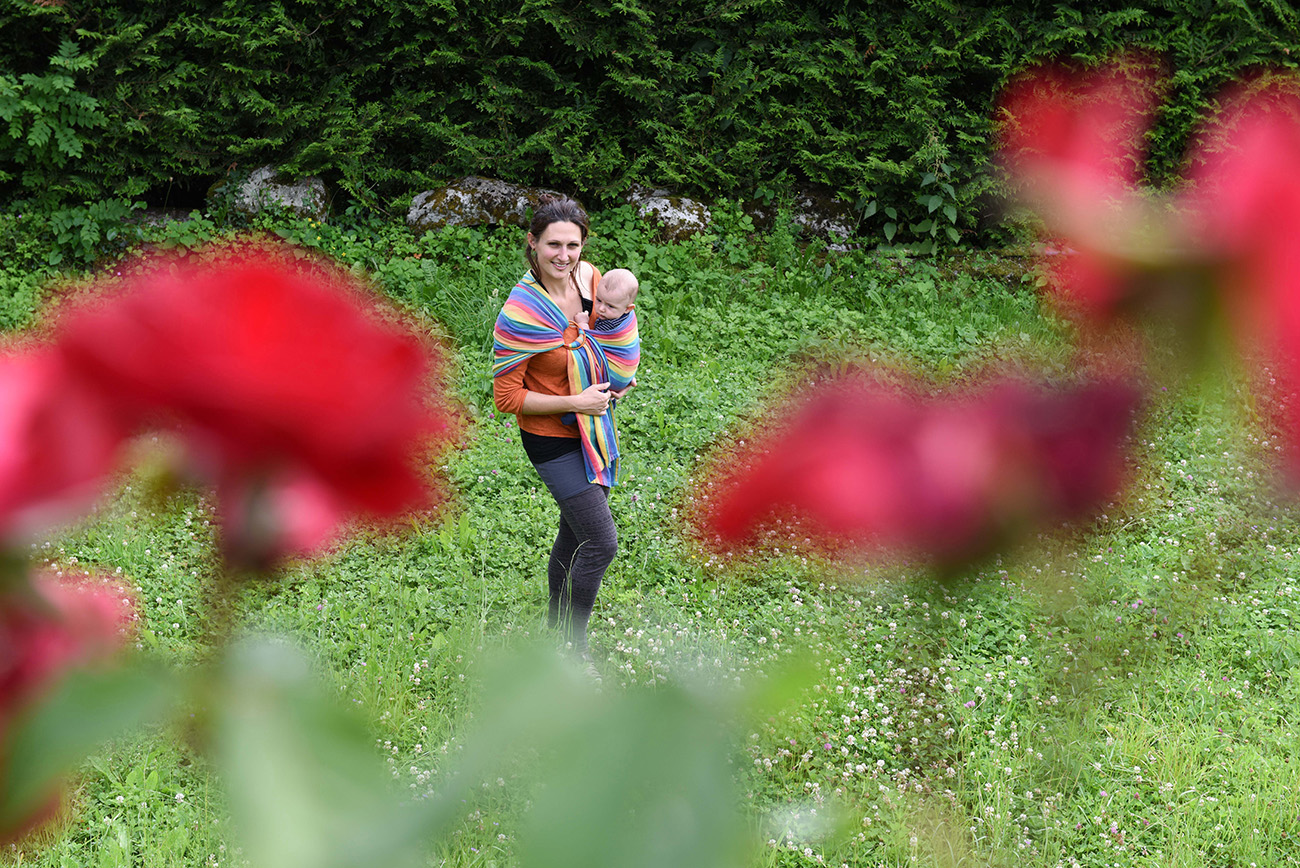 Low angle shot Behind red flowers blurred a mommy holding her young baby with a scarf