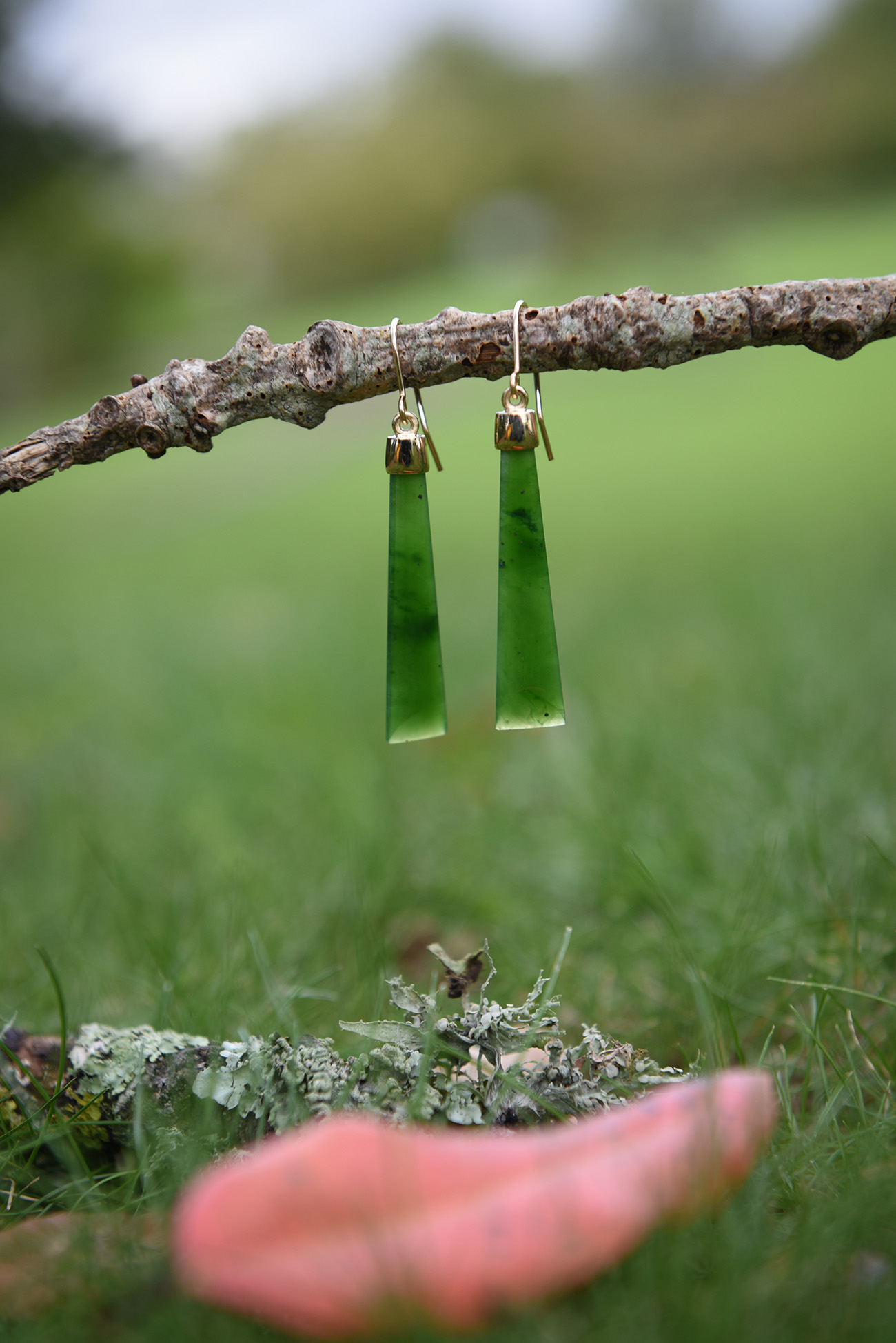 On a little branch greenstone earrings dangling with a blurred red leaf