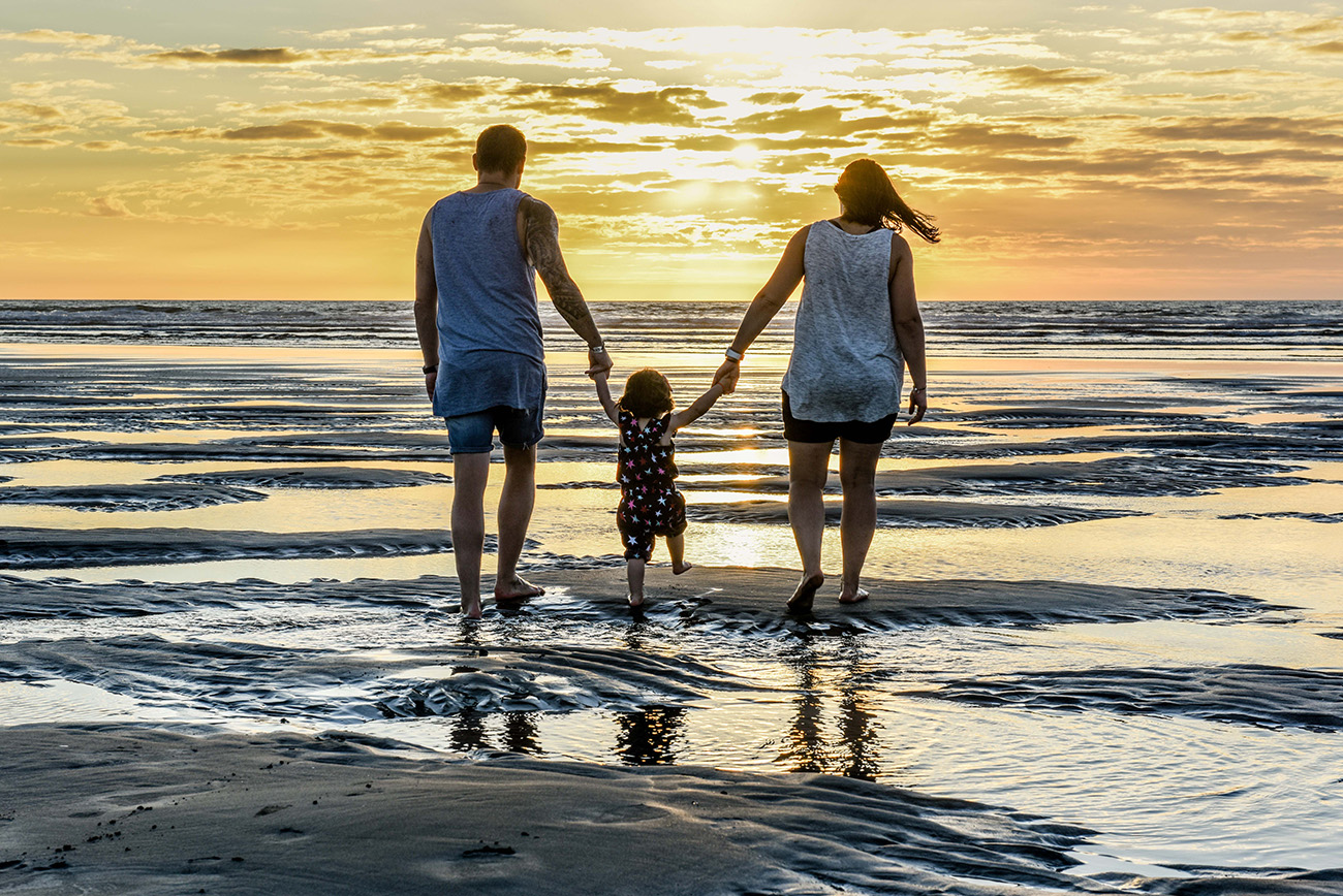 Family casts silhouette as they walk into sea on NZ beach at sunset