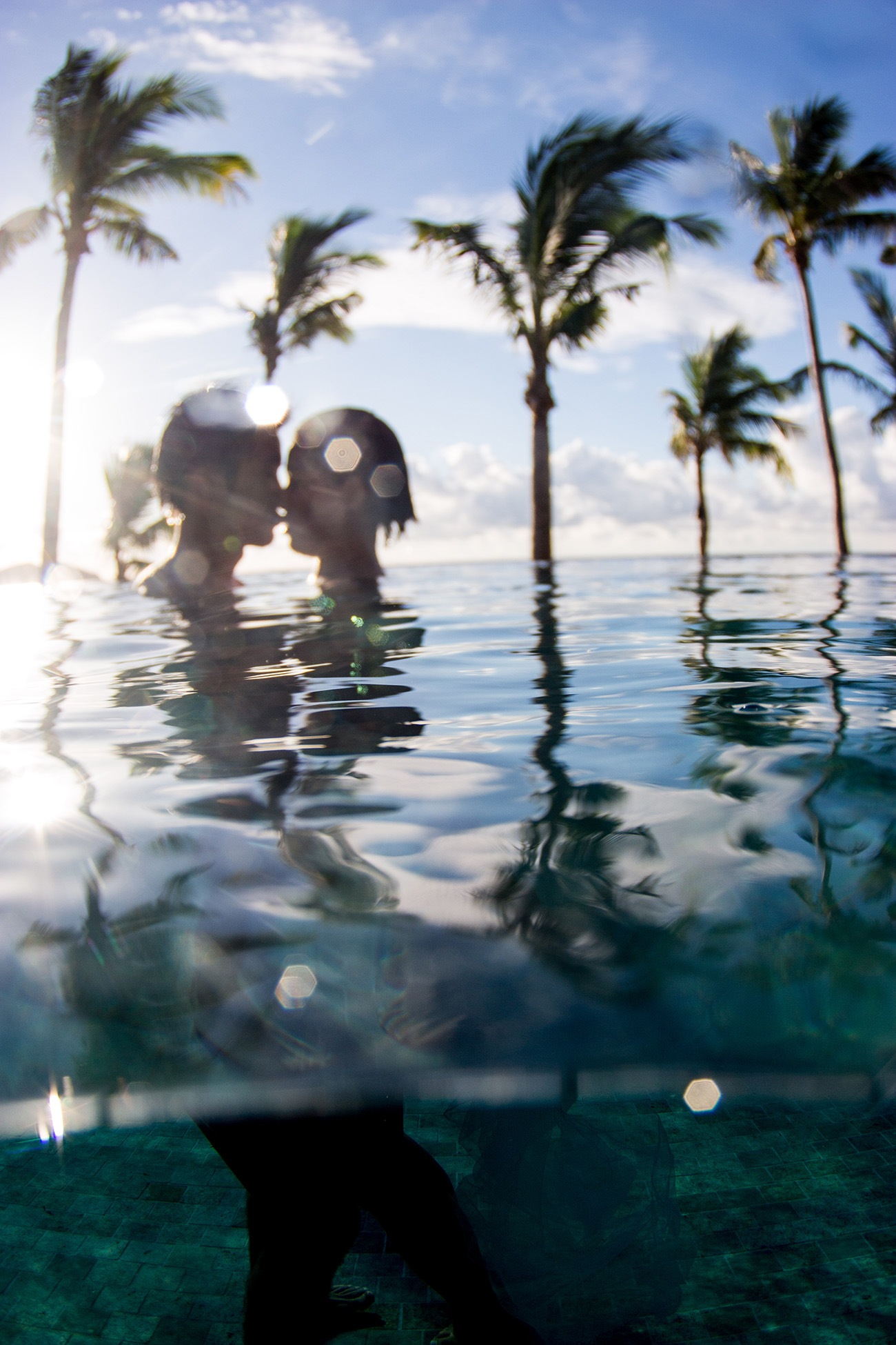 In Tokoriki island resort couple kissing with sun coming through and palm trees in Fiji by Anais Photography