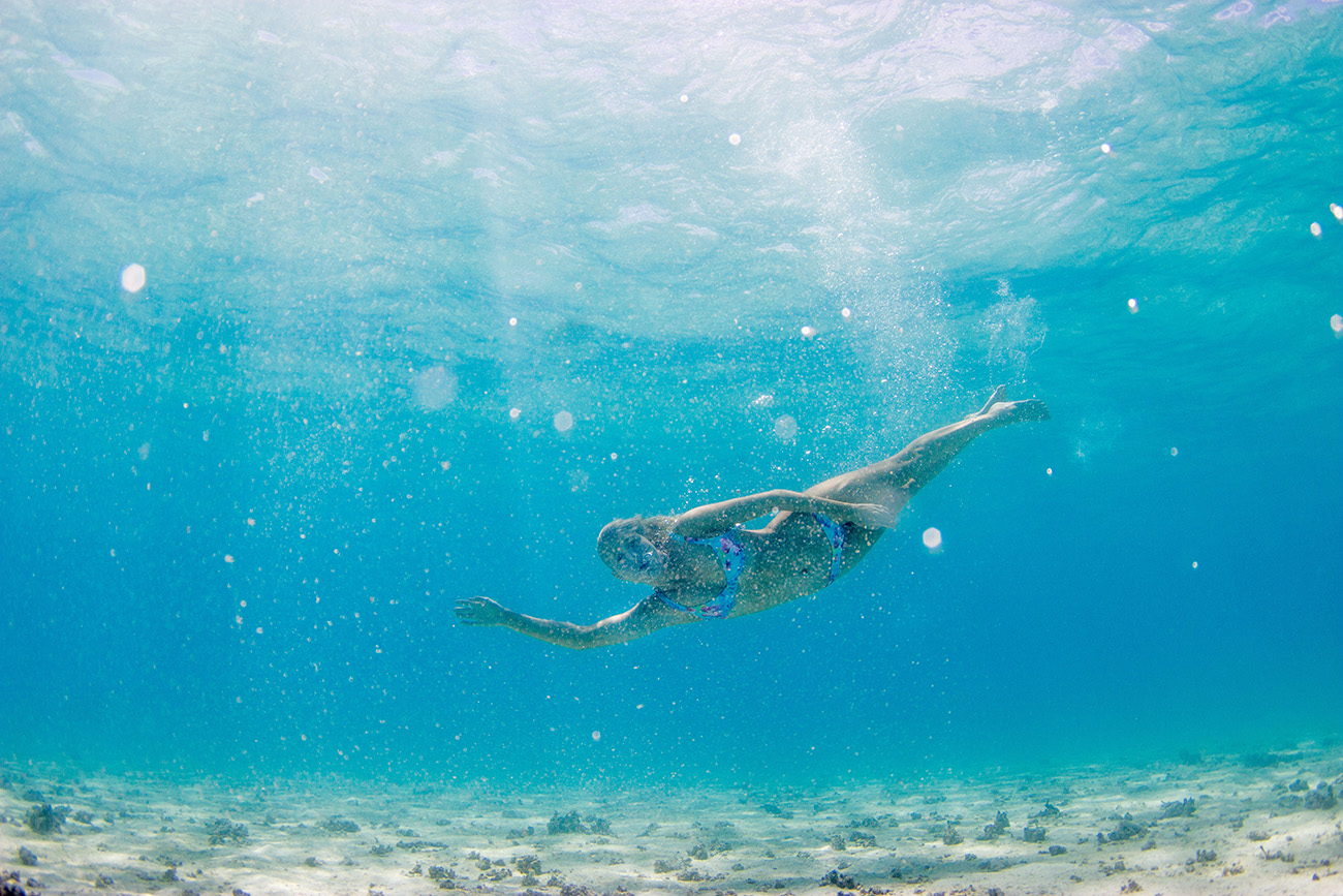 Woman swimming sideways underwater in the pure blue Fiji water