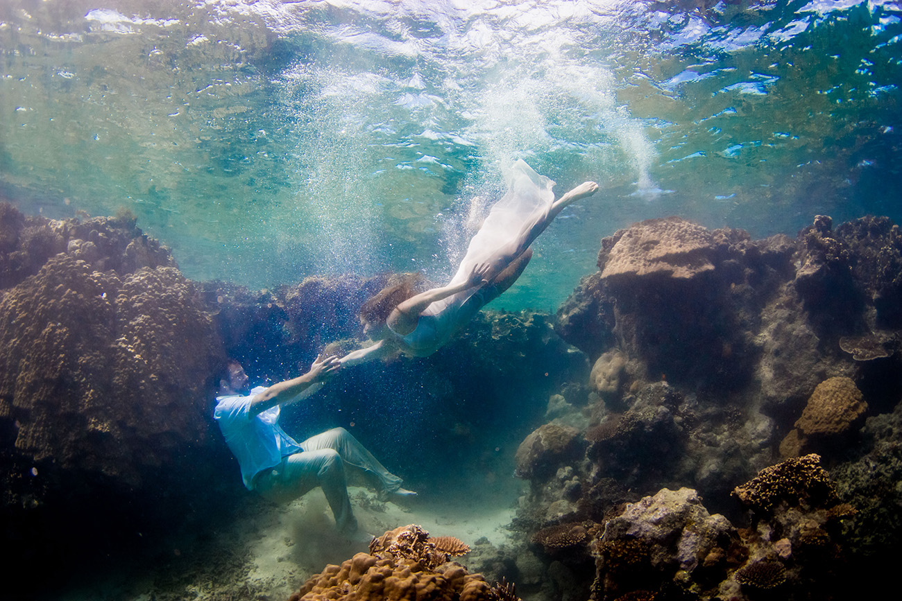 Couple swimming underwater by a coral wall