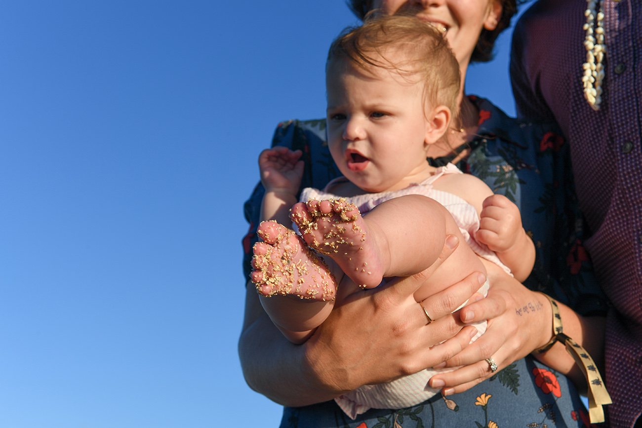 Baby with sandy feet carried against azure sky in Natadola beach Fiji