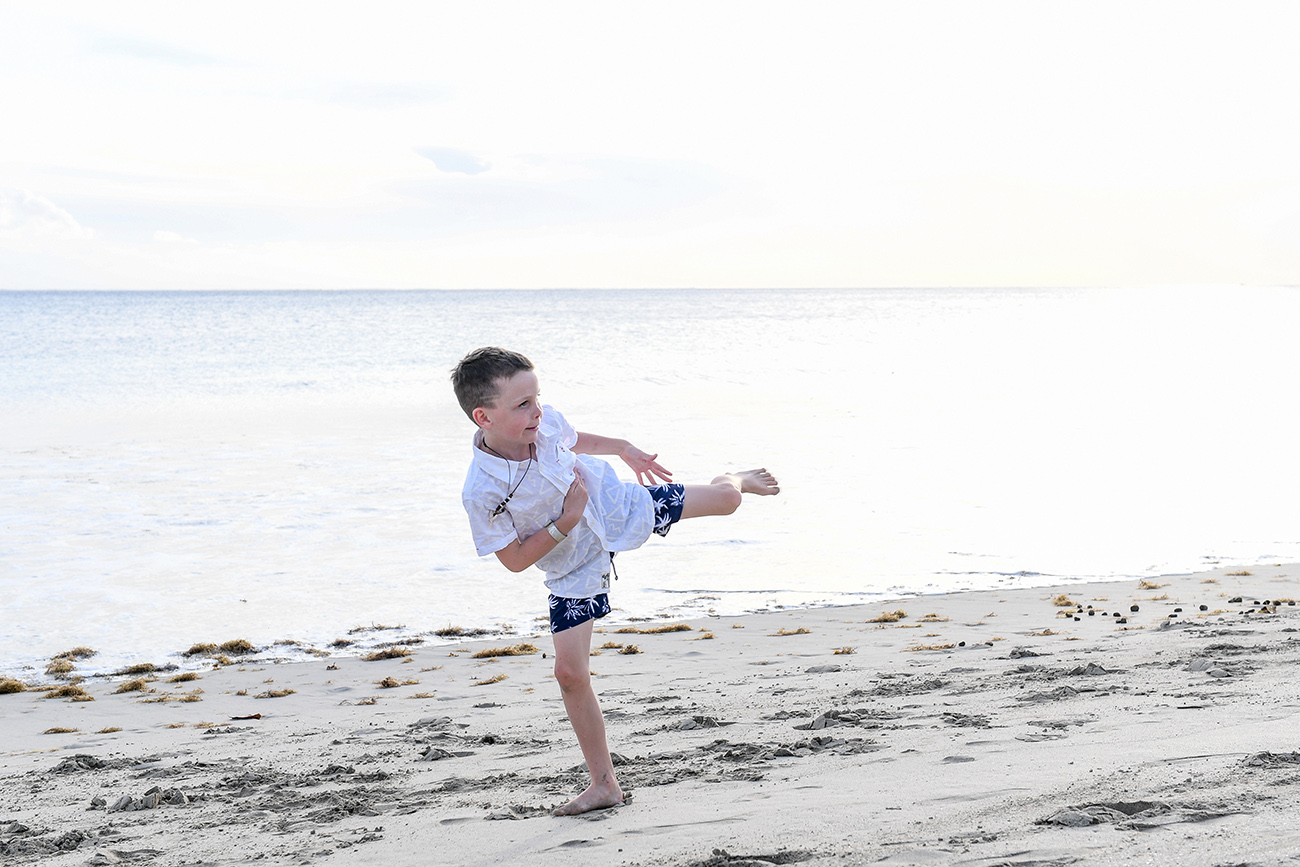Young boy does karate kick on the beach in Fiji