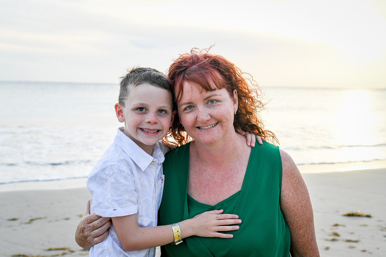 Red haired mum pauses with son on beach in Fiji