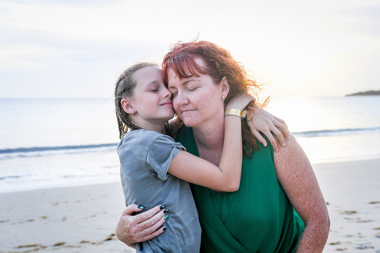 Braided daughter hugs red haired daughter on sunset