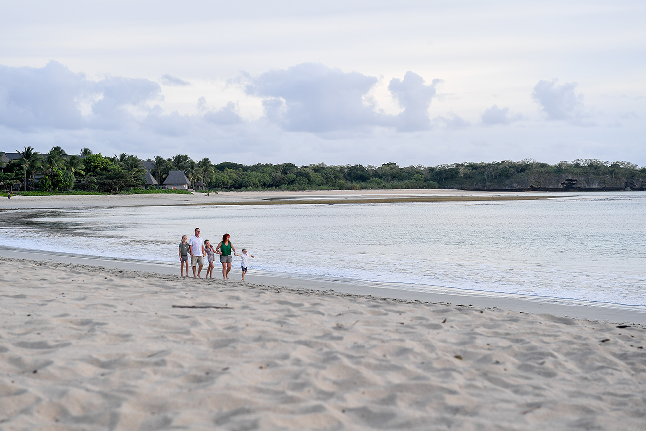 Wide shot of family strolling on beach in sunset in Fiji Natadola
